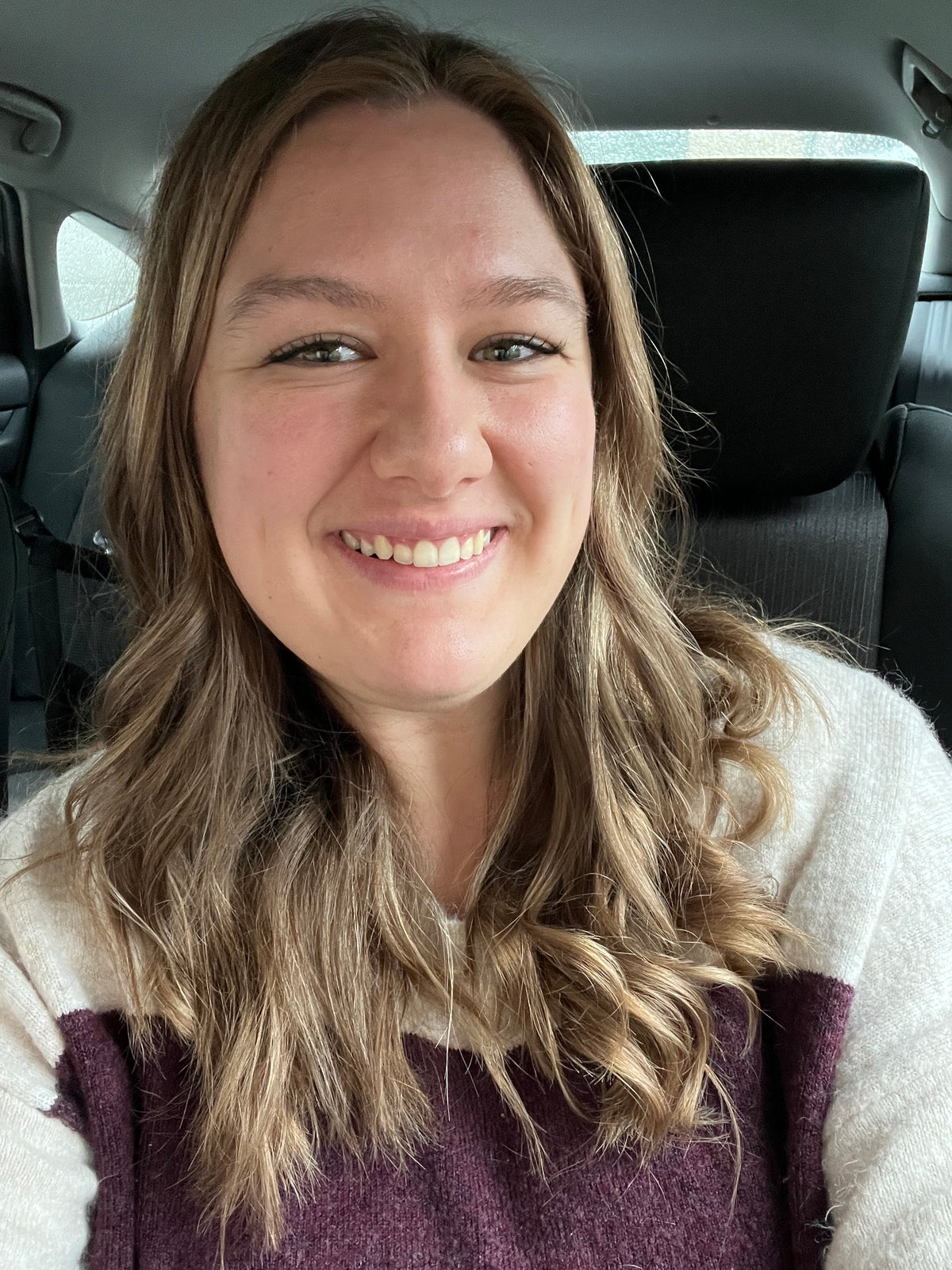 Woman with long blonde hair sitting inside a vehicle, wearing a plaid jacket.