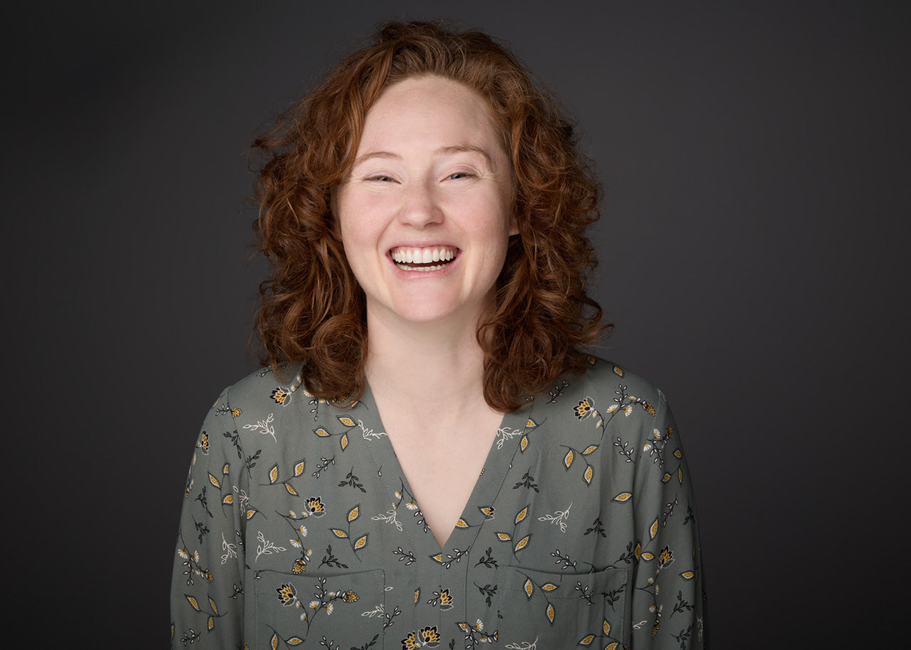 Woman with red hair wearing a patterned shirt against a dark background